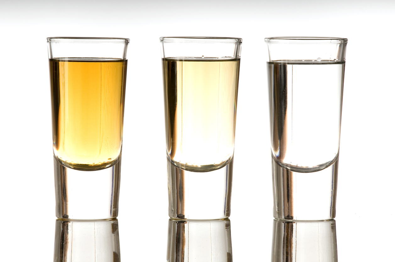 Three shot glasses filled with tequila are lined up on a white background, showcasing the distinct golden tequila color in each glass. The focus highlights the clarity and warm hue typical of quality tequila.